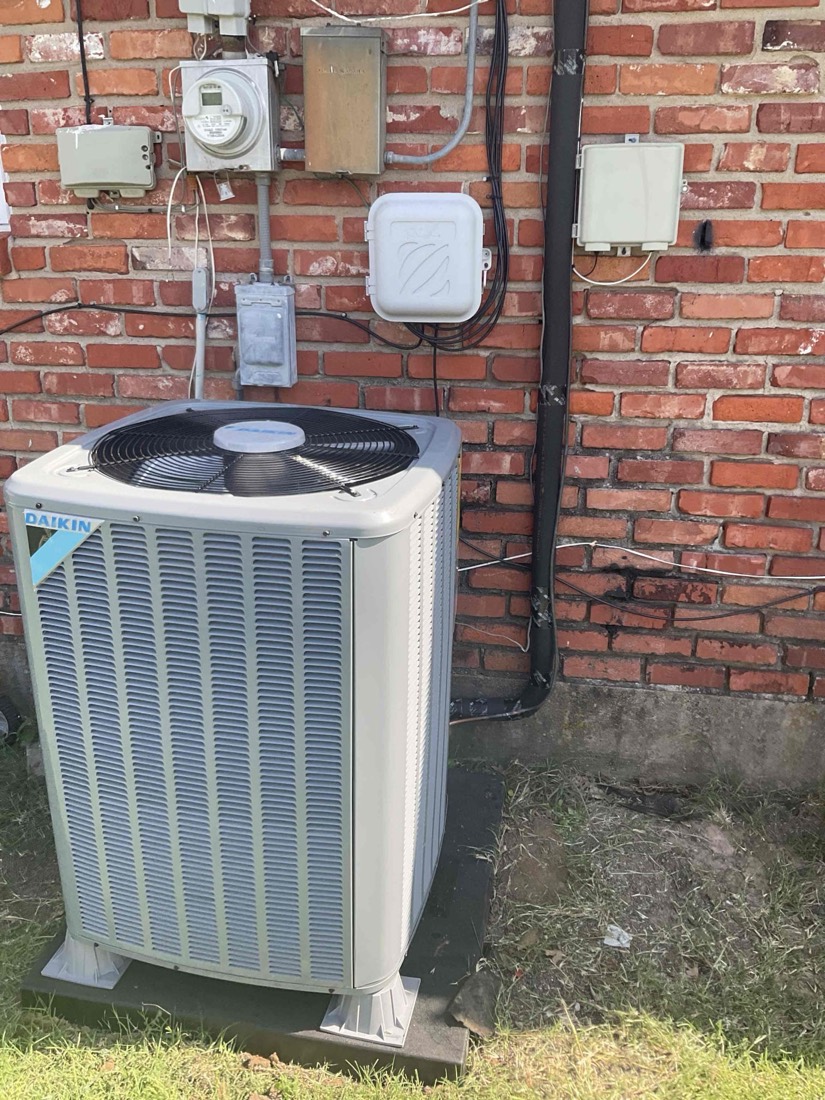 Daikin AC condenser unit with mounted electrical box on brick wall