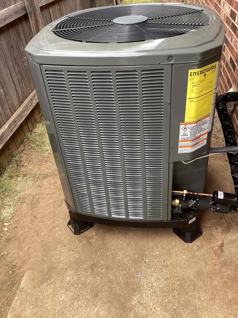 Energy Guide-labeled gray AC condenser unit on concrete pad with brick home background