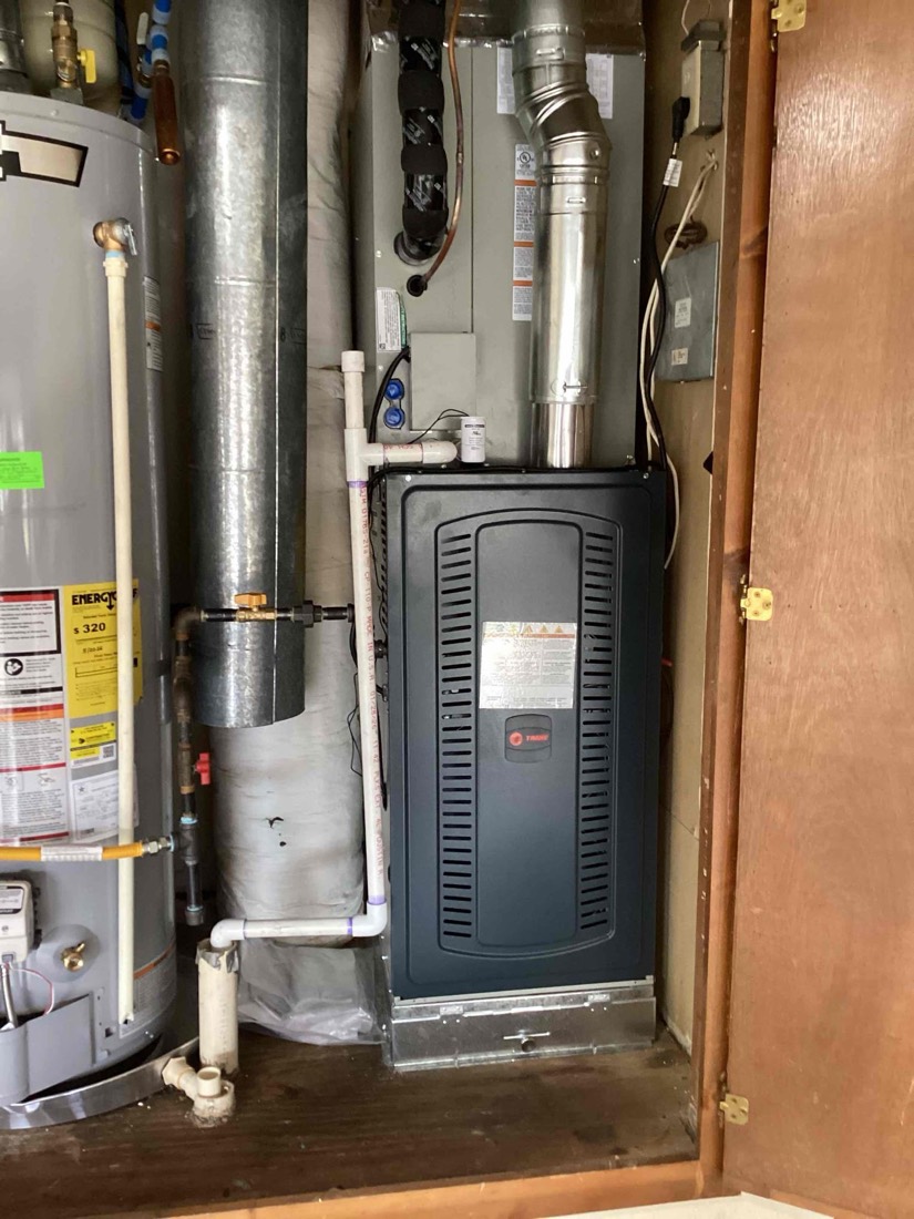 Interior view of newly installed furnace and black heat pump unit in utility closet