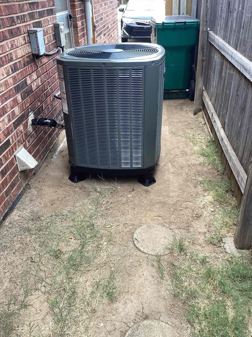 Gray air conditioning condenser unit installed against brick home with wooden fence
