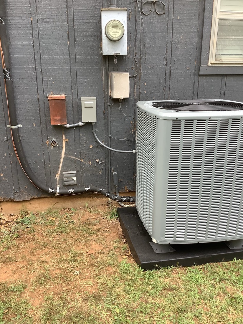 Installed AC unit with refrigerant lines and electrical connections on building exterior