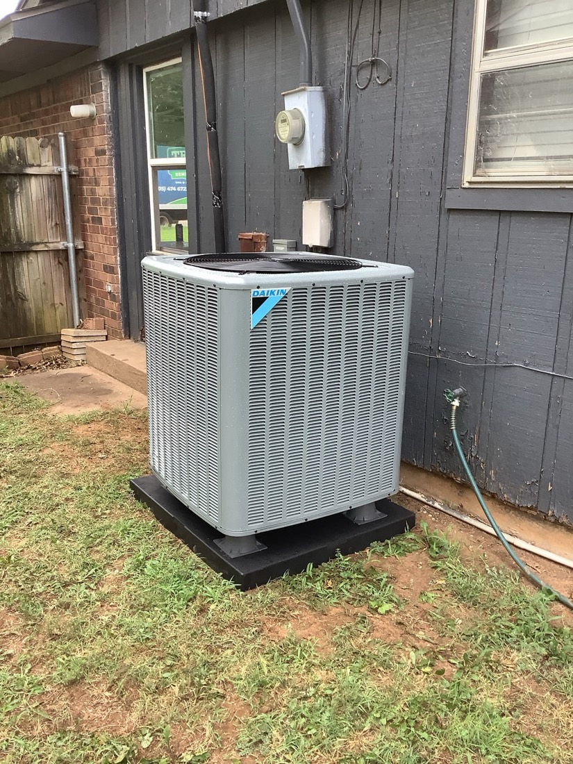 White Daikin air conditioner unit installed on black pad outside home