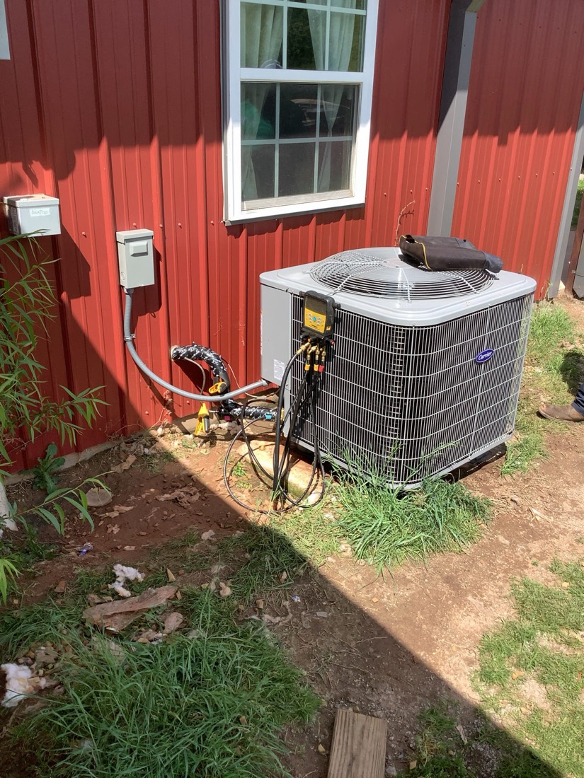 Newly installed outdoor air conditioning condenser unit against a red building with white window.