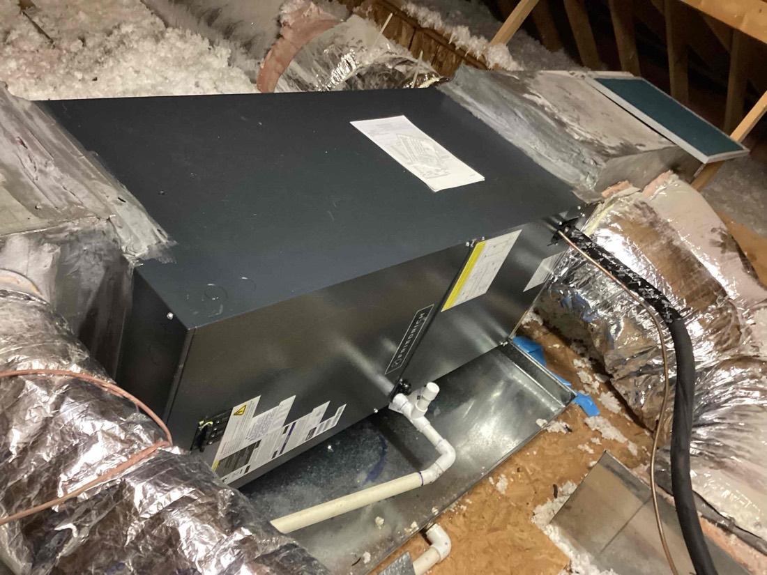 HVAC unit installed in attic with foam insulation and piping.