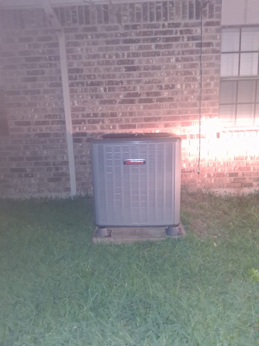 Installed air conditioning condenser unit on concrete pad against brick wall
