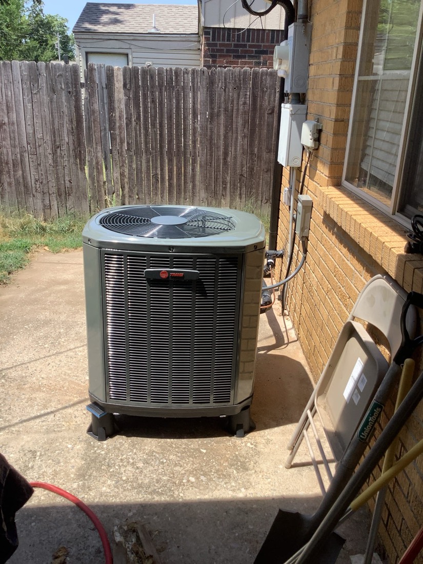 Outdoor AC condenser unit properly installed beside brick home
