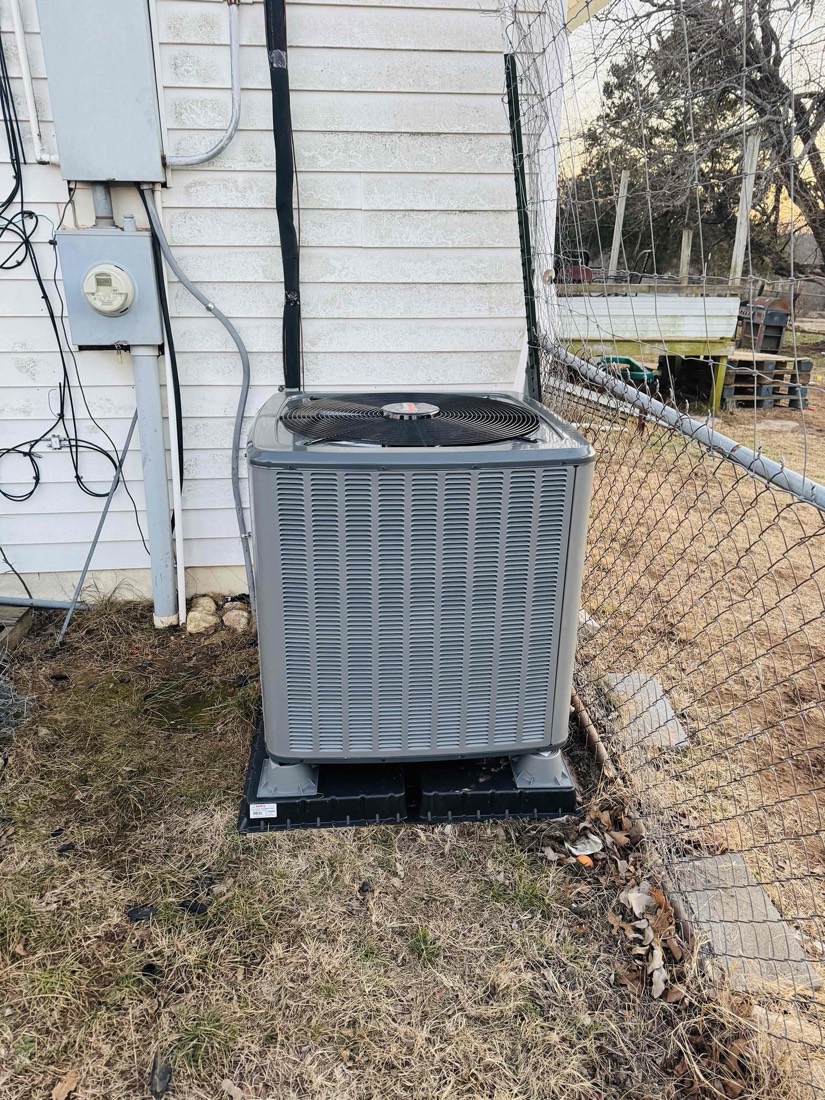 New gray AC condenser unit installed on concrete pad.