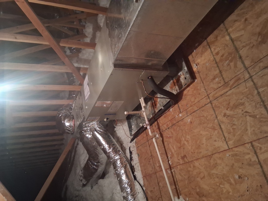 Air handler unit with silver ductwork in residential attic space.