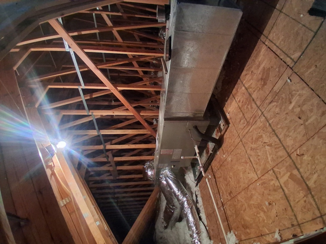 Metal ductwork and air handler unit in attic with exposed framing.