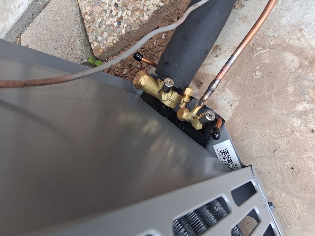 Heat pump outdoor unit with brass fittings and refrigerant lines.
