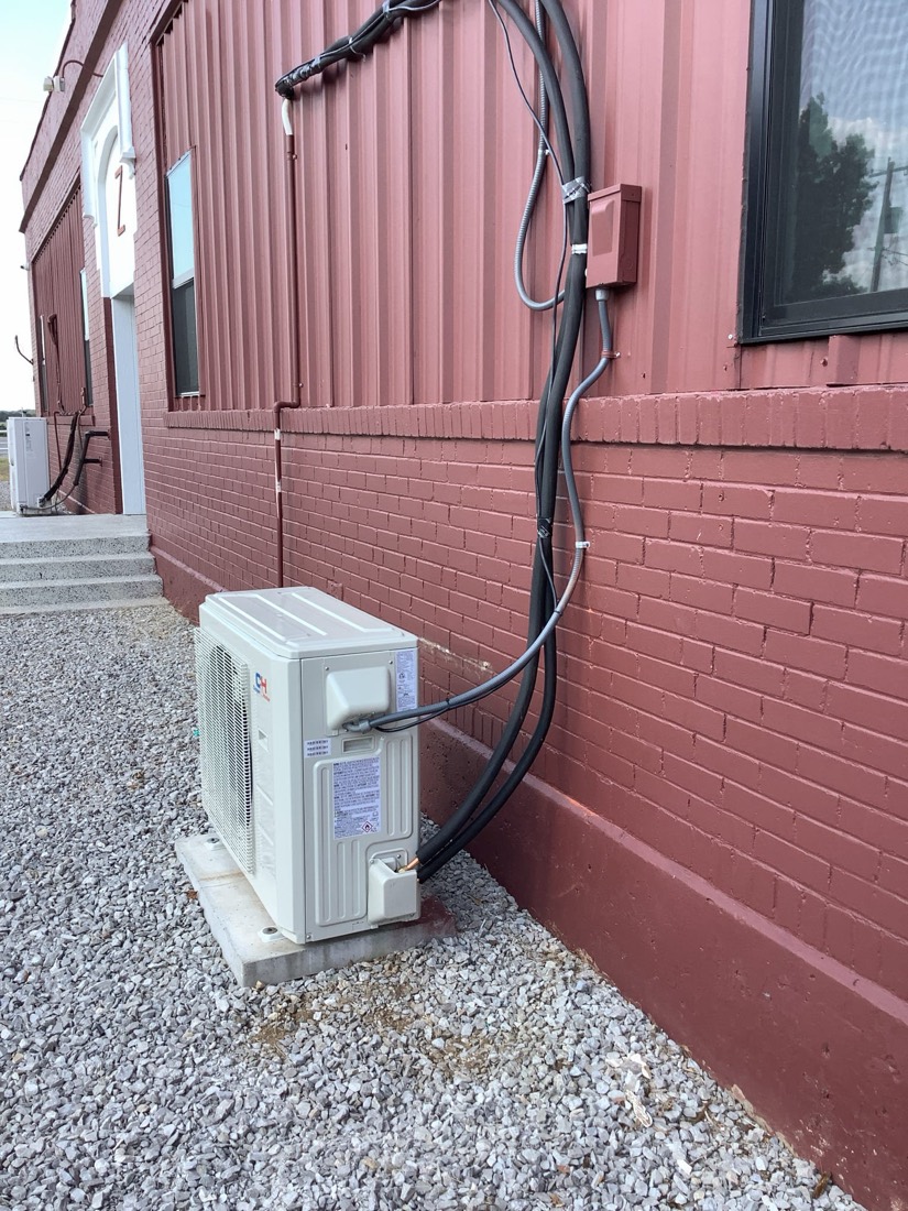 Newly installed outdoor mini-split unit with black refrigerant lines running up red brick wall
