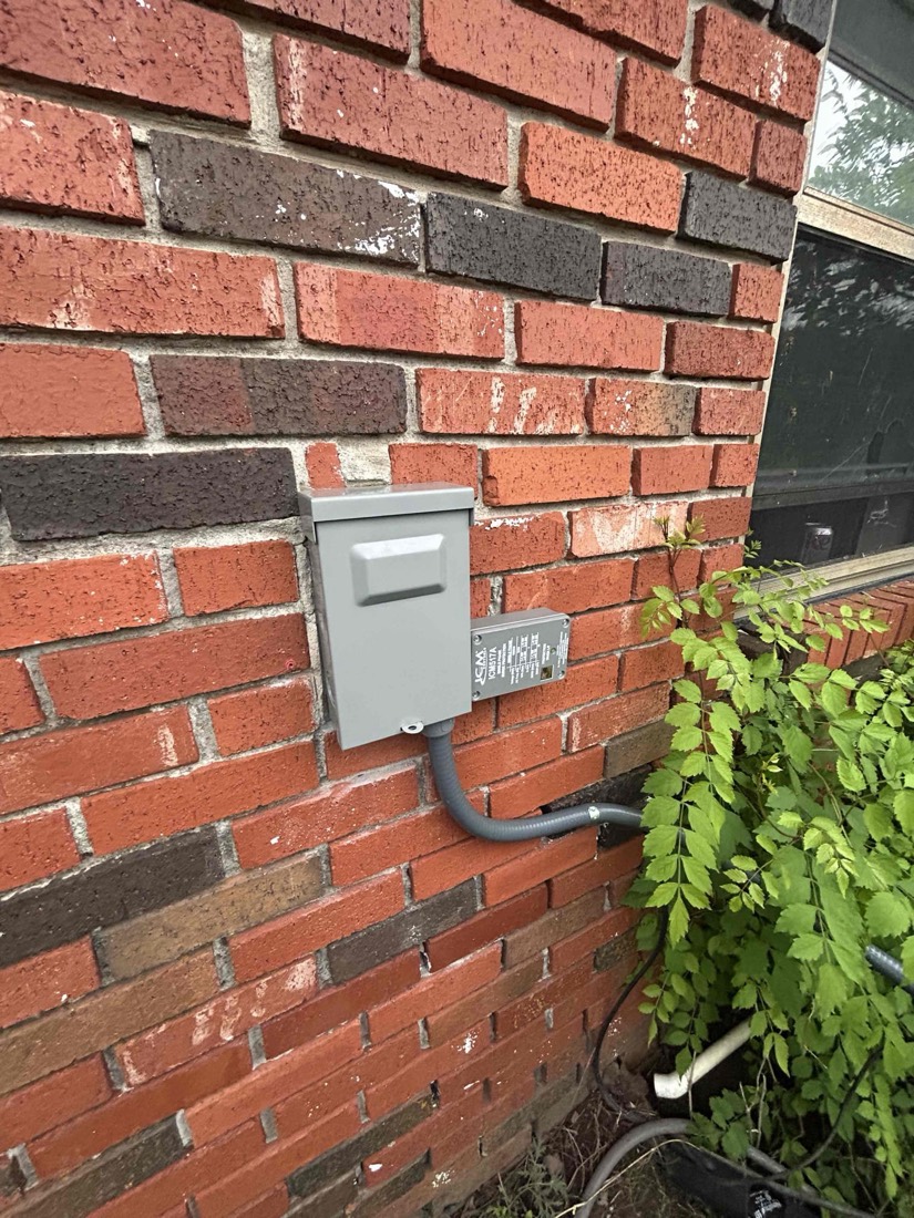 Outdoor electrical service panel on brick wall.