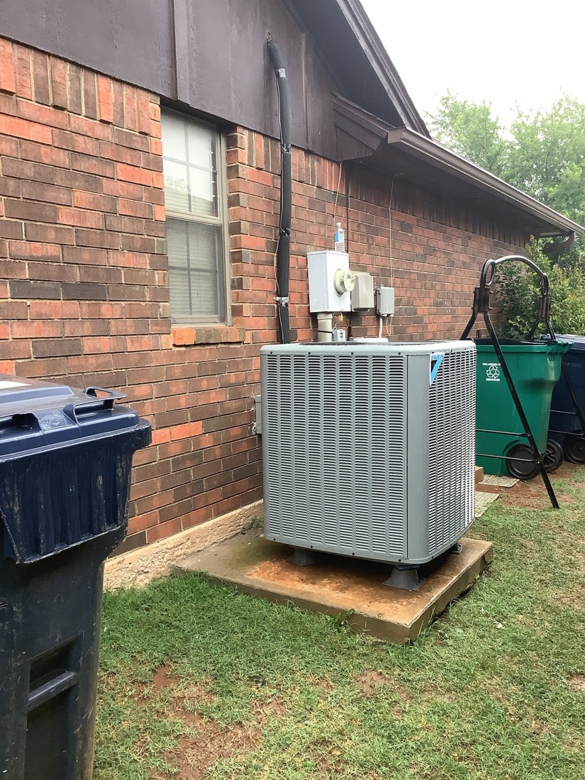 Newly installed air conditioning unit mounted on concrete pad beside brick home.