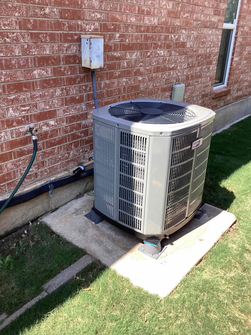 Newly installed AC condenser unit on concrete pad against brick wall.