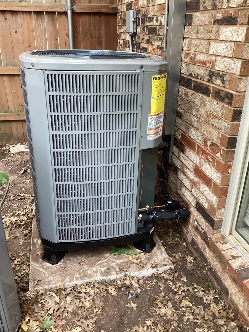 Newly installed outdoor air conditioning unit secured to foundation beside brick home
