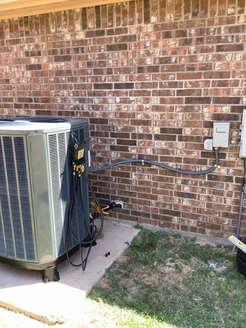 Installed AC condenser with copper line set and electrical connections on brick wall
