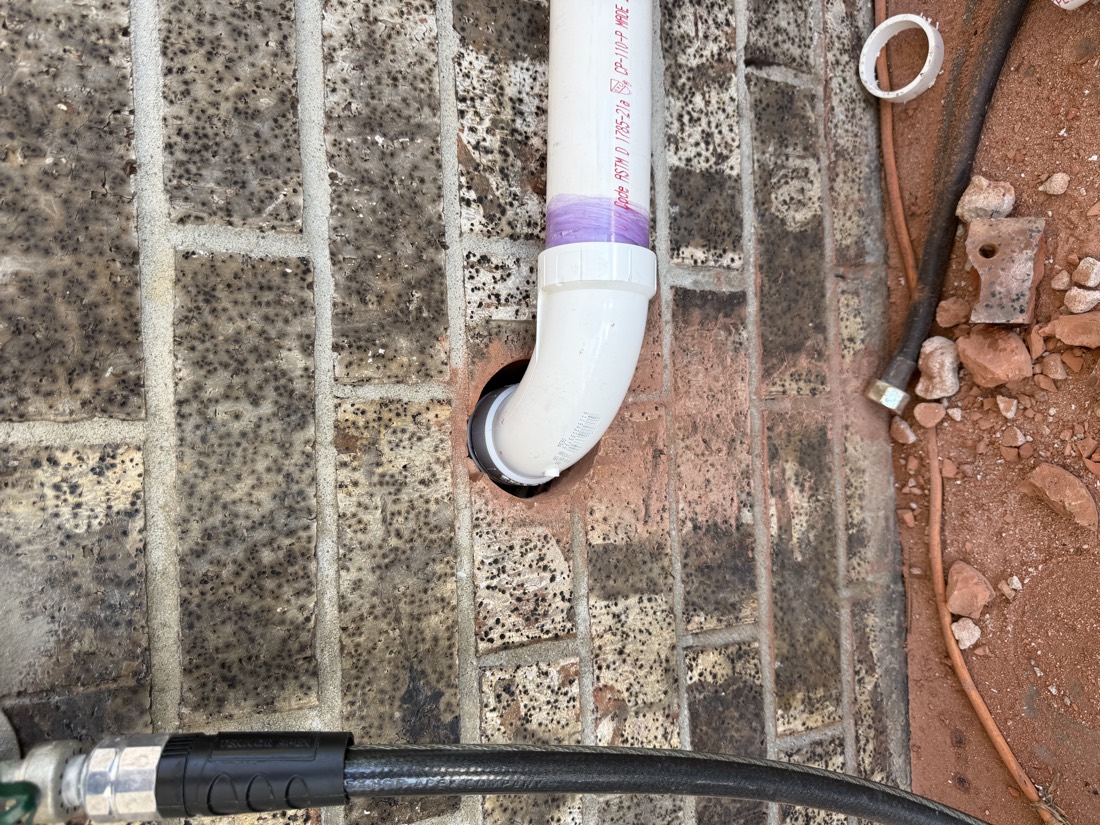 White PVC condensate drain vent installed through brick foundation wall.