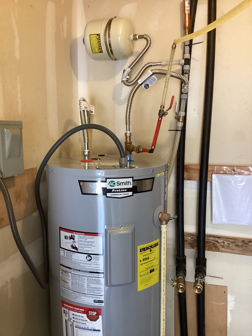 Electric water heater with connected piping, expansion tank, and relief valve