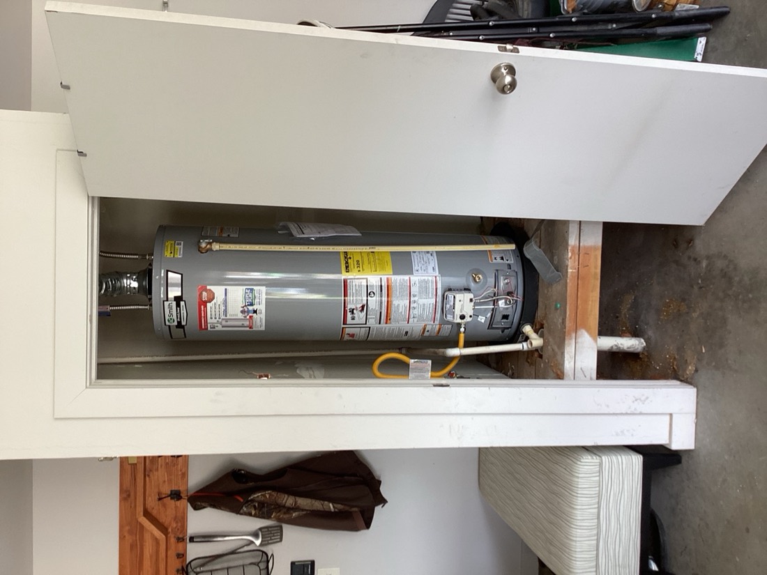 Gas water heater installed in utility closet with white piping.