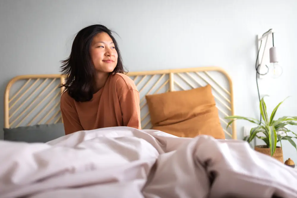 Humidity effects on your HVAC system - Happy young asian woman sitting on bed after waking up in the morning in cozy bedroom at home.